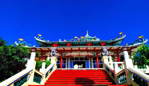 Traditional Chinese temple with red stairs and green-tiled roof under blue sky in Cebu City