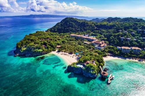 Aerial view of Boracay Island with turquoise waters, white sand beach, dense tropical forest, and beachfront resorts nestled