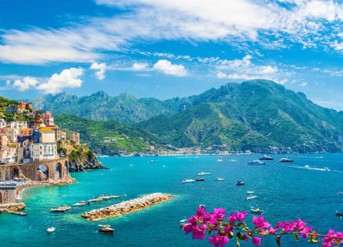 Colorful village of Atrani on Amalfi Coast with turquoise water, boats, and pink flowers in foreground