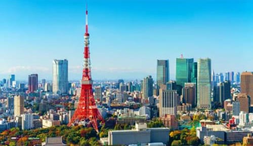 Tokyo skyline with red Tokyo Tower at center surrounded by modern skyscrapers and clear blue sky