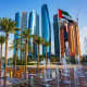 Abu Dhabi skyline with modern skyscrapers, UAE flag, palm trees, and fountain plaza with clear blue sky