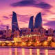Baku skyline at sunset with illuminated Flame Towers reflected in Caspian Sea, historic buildings along waterfront