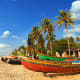 Colorful traditional fishing boats beached on sandy shore with palm trees and blue sky in Goa