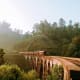 Red train crossing a historic arched bridge over a misty valley surrounded by lush green forested hills in Kandy, Sri Lanka