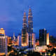 Petronas Twin Towers illuminated at dusk in Kuala Lumpur skyline with surrounding buildings and cityscape