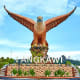 Large golden eagle monument with outstretched wings above Langkawi sign and ornamental base against blue sky