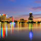 Orlando skyline at dusk with illuminated buildings and colorful fountain reflecting in Lake Eustis water