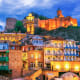 Tbilisi old town at dusk with colorful buildings and illuminated Narikala Fortress on the hill above