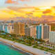 Aerial sunset view of Miami Beach with turquoise ocean, sandy shore, high-rise hotels and residential buildings, and city sky