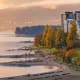Vancouver waterfront at sunset with high-rise buildings, beach, autumn trees, and North Shore mountains