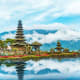Pura Ulun Danu Bratan temple with tiered pagoda reflected in calm lake water, mountains and clouds in background, Bali