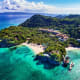 Aerial view of Boracay island showing tropical beach, turquoise waters, dense green forest, and limestone cliffs under blue s