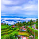 Aerial view of Darjeeling hillside village with green terraced fields, traditional houses with red roofs, and misty mountain 