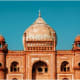Historic red sandstone mosque with large dome and minarets against clear blue sky in Delhi, India
