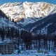 Snow-covered Himalayan valley with pine forests and a building nestled below snow-capped mountain peaks in Manali