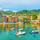 Colorful waterfront village with boats in turquoise water, hillside buildings, and green mountains, Cinque Terre Italy