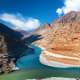 Aerial view of turquoise glacial lake surrounded by barren mountains in Leh, India with snow-capped peaks and clear blue sky