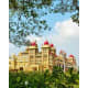 Mysore Palace with golden yellow walls and red domed turrets surrounded by green trees under blue sky