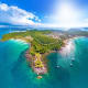 Aerial view of Phu Quoc island with turquoise waters, sandy beaches, forested hills, and moored boats under blue sky