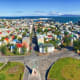 Aerial view of Reykjavik cityscape with harbor, residential neighborhoods, and mountains across the bay under clear blue sky