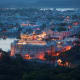 Udaipur cityscape at dusk with illuminated palace on hilltop overlooking lake and surrounding buildings