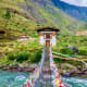 Traditional Bhutanese temple with painted prayer flags spanning across turquoise river in Paro valley mountains