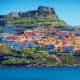 Colorful hillside village with castle ruins overlooking blue sea in Sardinia, Italy