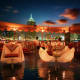 Rooftop dinner setup with city skyline and illuminated building at dusk, elegant table settings with white linens overlooking
