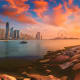 Dubai skyline at sunset with Burj Khalifa, modern skyscrapers, boats on water, and observation wheel on horizon