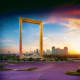 Giant golden frame structure at sunset with Dubai skyline and city buildings visible through the center opening