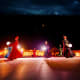 Performers in traditional red and colorful robes dancing at night in an illuminated desert camp with warm lighting and dark s