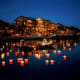 Illuminated lanterns floating on water at dusk with historic yellow buildings lit up along the waterfront in Hoi An Ancient C