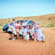 Large group of tourists posing enthusiastically in desert sand with 4x4 vehicle and sandy dunes in background during Ras Al K
