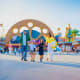 Family walking through Motiongate Dubai theme park entrance with large paw print archway and colorful attractions in backgrou
