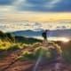 Hiker standing on mountain trail at sunrise overlooking sea of clouds and Mount Batur volcano at dawn