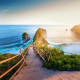 Wooden railing pathway overlooking Kelingking Beach with dramatic rock formations and turquoise ocean waters at sunset, Nusa 