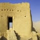 Ancient mud brick fortress with single entrance opening, set against desert landscape and clear blue sky in Ras Al Khaimah
