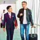 Business travelers walking through modern airport terminal with luggage and other passengers in background