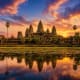 Angkor Wat temple complex reflected in water at sunset with palm trees and golden sky in Cambodia