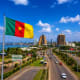 Cameroon flag flying over Yaoundé cityscape with modern buildings and busy street traffic
