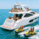 Luxury white yacht with passengers and two yellow jet skis in turquoise waters near rocky coastline