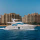 Luxury white motor yacht anchored in turquoise water with modern beige apartment buildings in background under clear blue sky