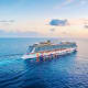 Large modern cruise ship sailing on calm turquoise ocean water at sunset with clouds in sky