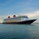 Large modern cruise ship with white upper decks and black hull sailing on calm blue water under cloudy sky