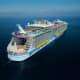 Aerial view of a large modern cruise ship on blue ocean waters with white superstructure and yellow hull stripe