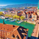 Aerial view of Zurich with turquoise river, historic church spires, red-roofed buildings, and Alps mountains in background