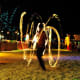 Fire dancer performing with glowing poi at nighttime beach festival with audience seated around sandy arena