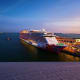 Large cruise ship docked at port during twilight with illuminated hull and calm blue waters
