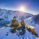 Ancient stone churches with golden domes on snow-covered island surrounded by frozen lake and snow-capped Caucasus mountains 