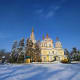 Yellow Orthodox cathedral with golden domes surrounded by snow-covered evergreen trees under clear blue sky in winter